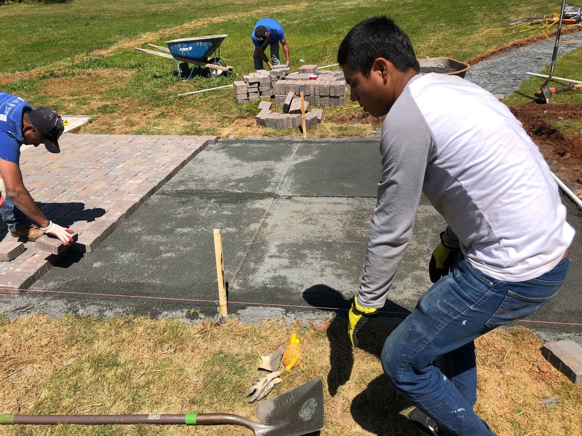 Workers pouring and smoothing a concrete slab outdoors on a grassy site
