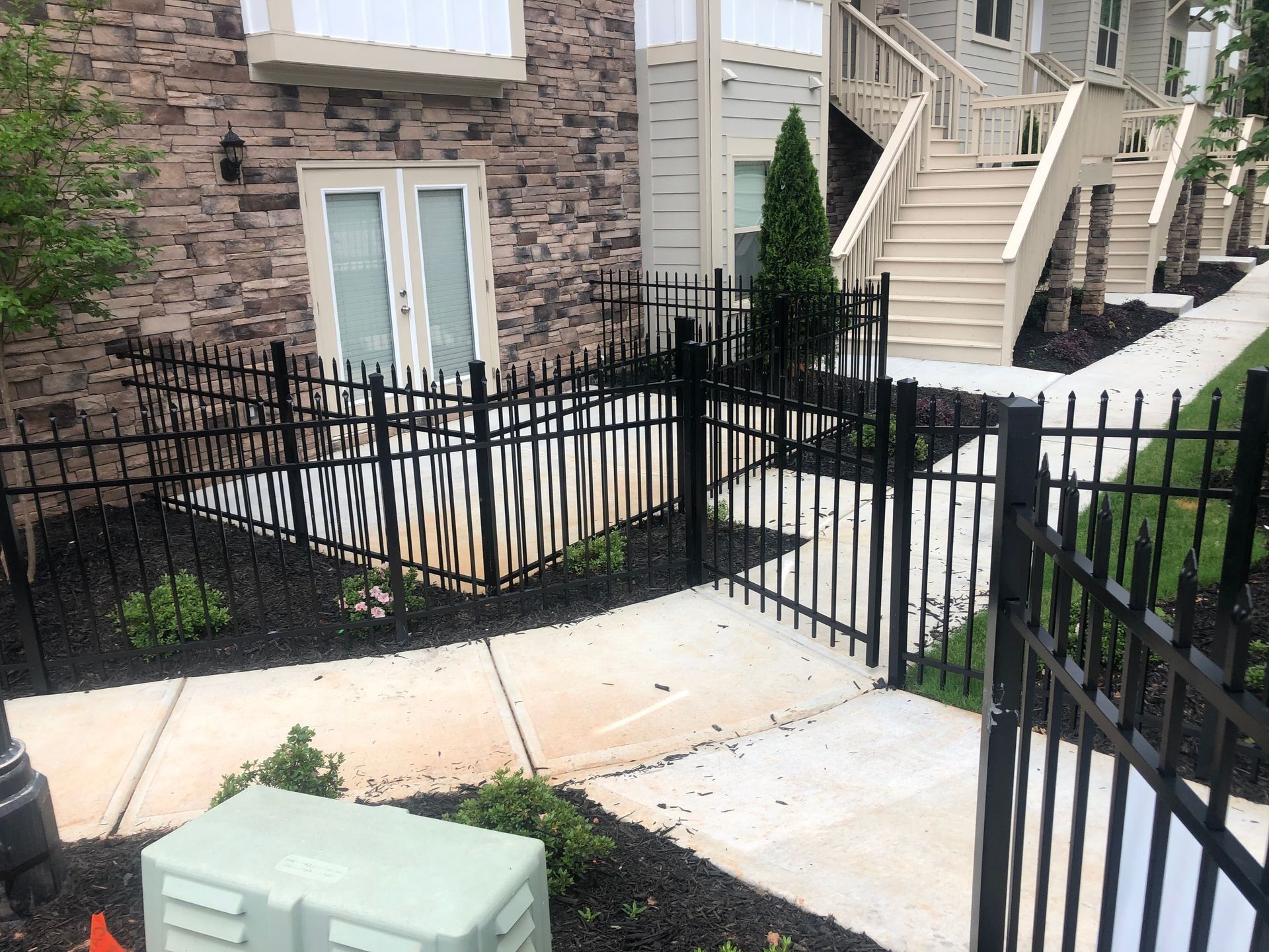Apartment walkway with black iron fencing, concrete path, and stone building exterior with stairs and shrubs