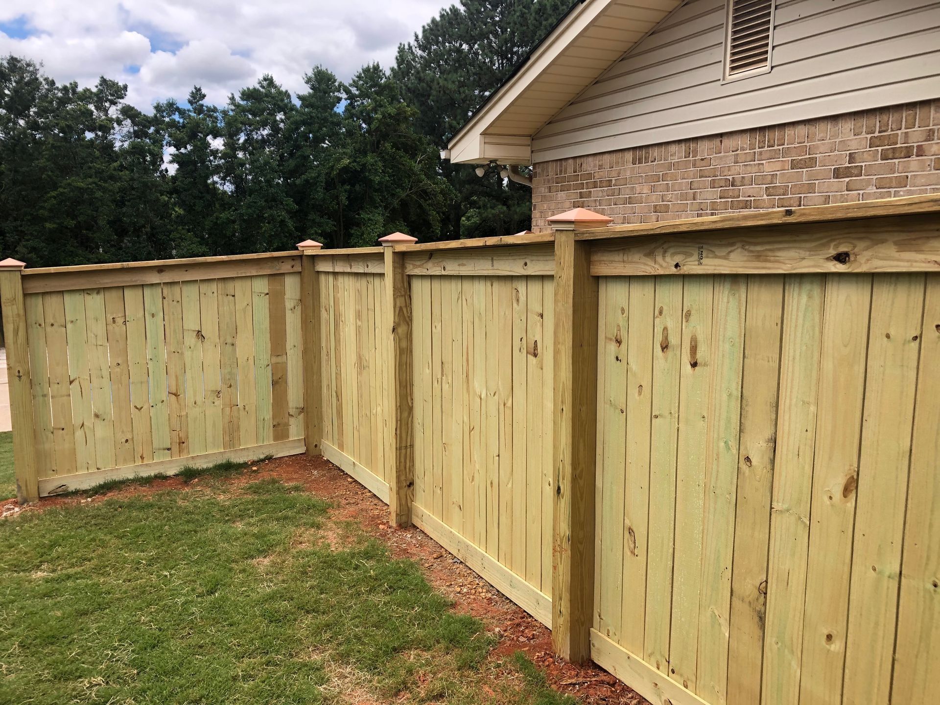 Wooden privacy fence enclosing a backyard corner beside a house under a cloudy sky