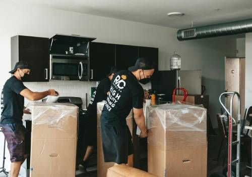 Three men moving appliances in boxes with wraps.