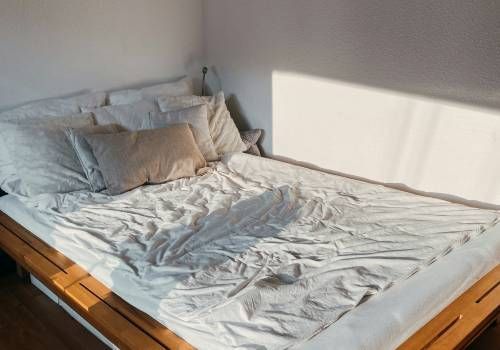 An image of a bed with white sheets and one brown pillow.