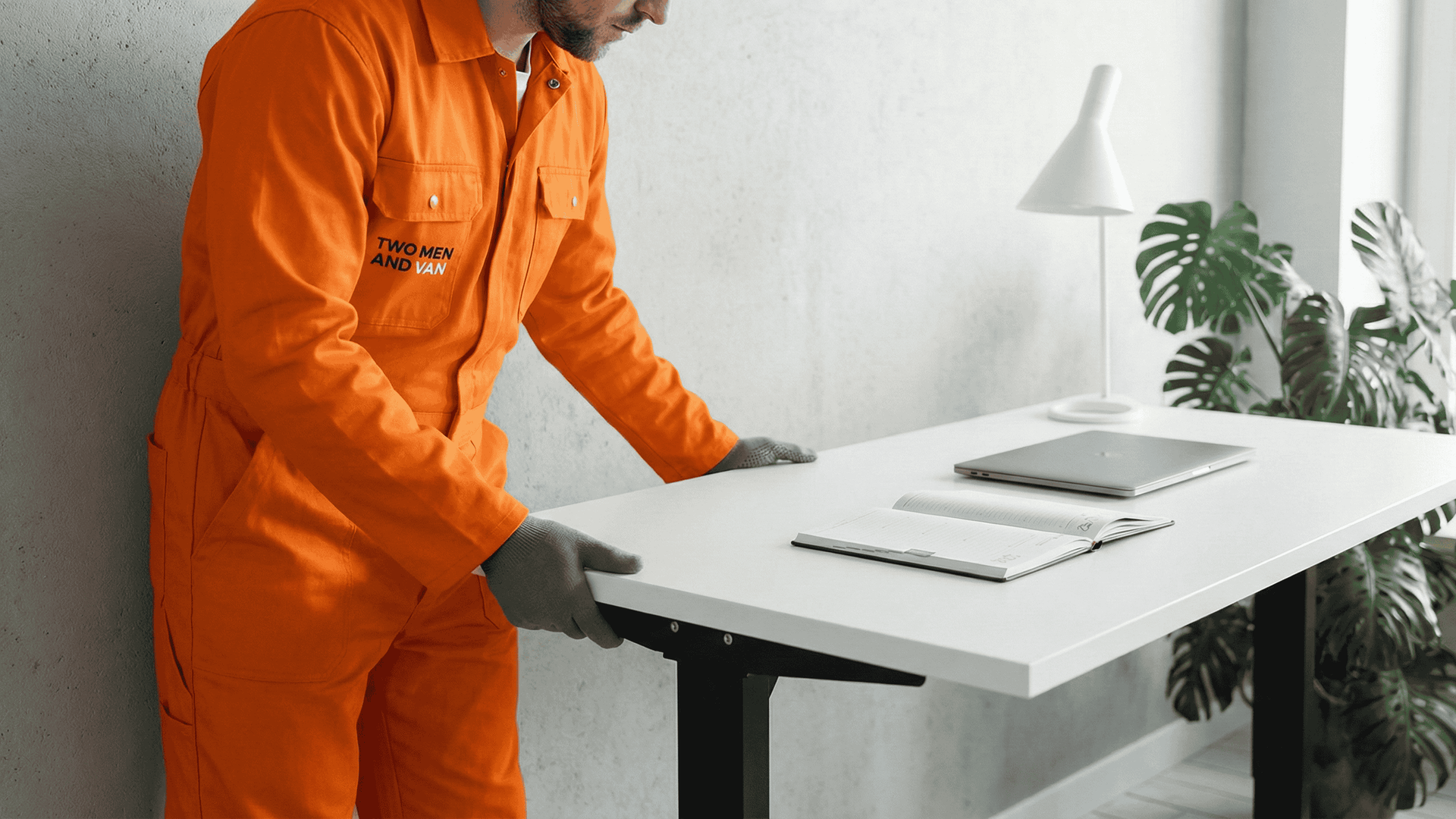 Mover in orange jumpsuit positioning a desk in a small home office setup