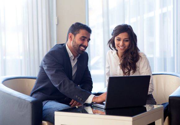 Un hombre y una mujer están sentados en una mesa mirando una computadora portátil.