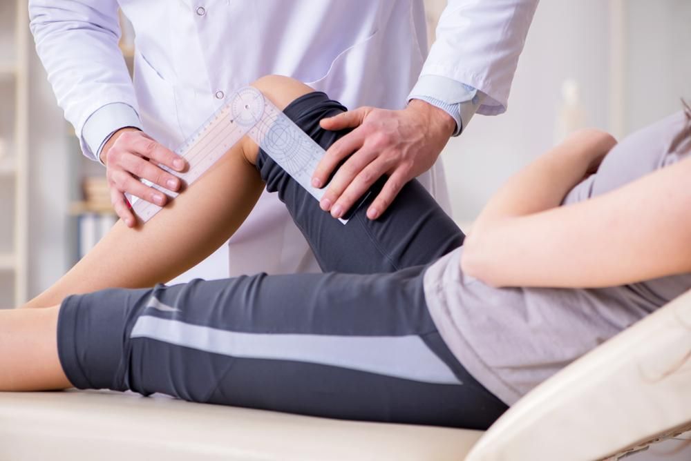 A Doctor Is Examining A Patient's Leg In A Hospital — Port Macquarie Physio & Pilates In Port Macquarie, NSW