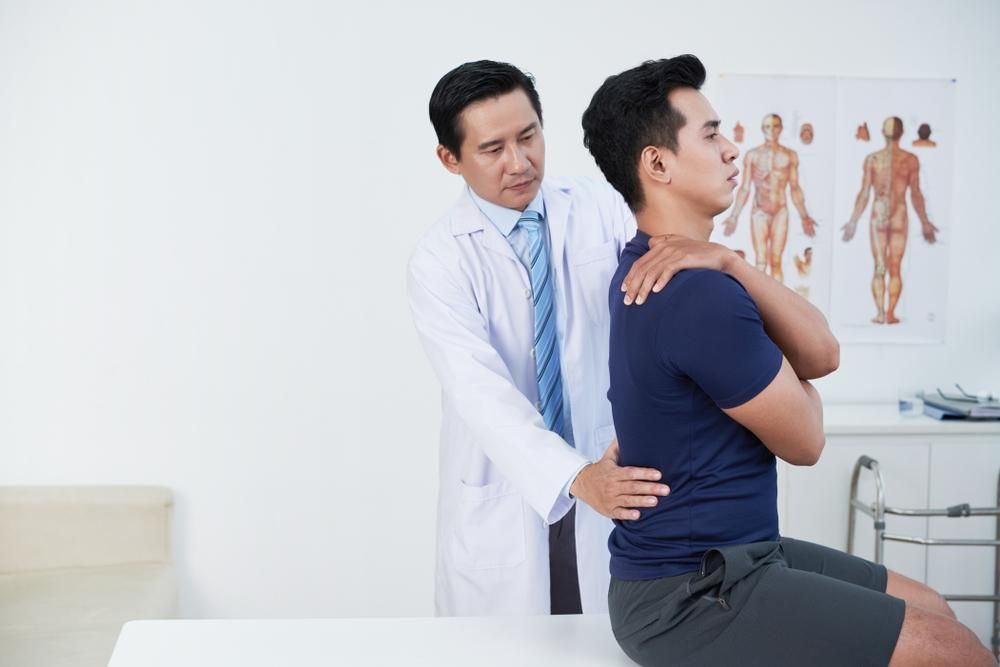 A Doctor Is Examining A Man's Back In A Hospital — Port Macquarie Physio & Pilates In Port Macquarie, NSW
