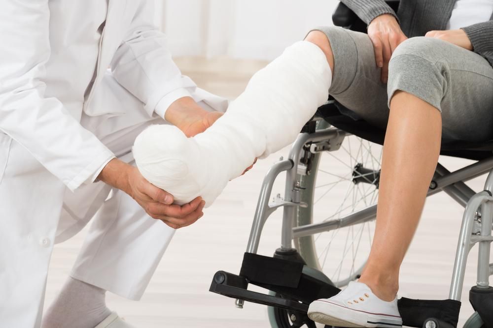 A Woman In A Wheelchair Is Getting Her Leg Cast Held By A Doctor — Port Macquarie Physio & Pilates In Port Macquarie, NSW
