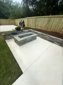 A man is pushing a wheelbarrow in a backyard next to a fire pit.