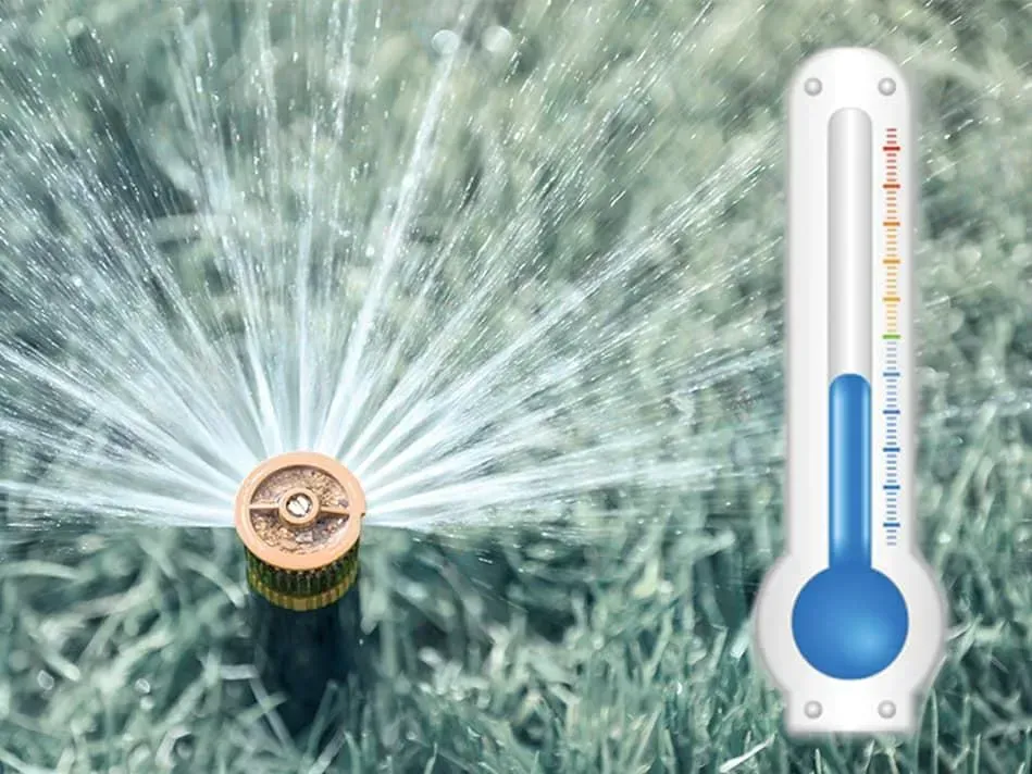 A sprinkler is spraying water on a lawn next to a thermometer.