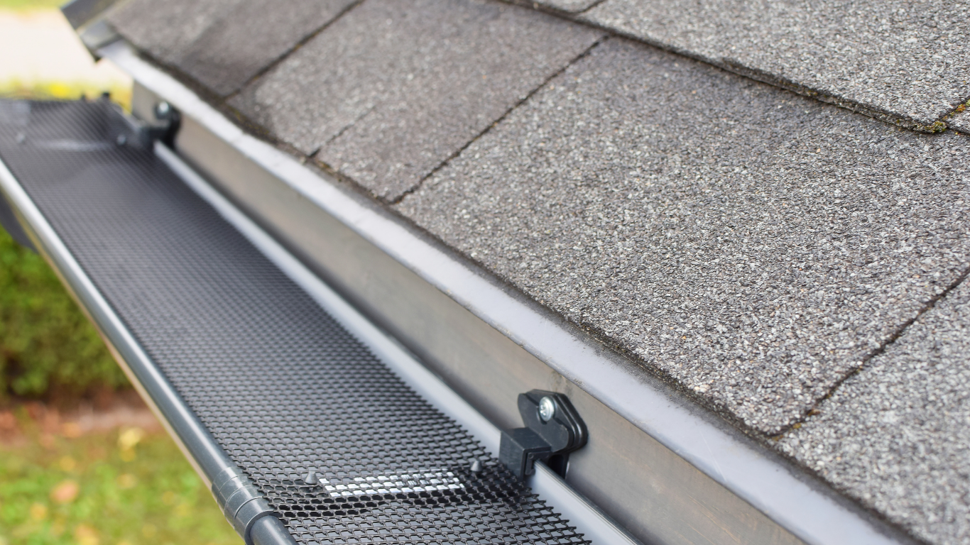 Roof gutter with a black gutter guard beside gray shingles.