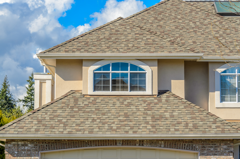 Suburban house roof with beige siding and arched window under a blue sky