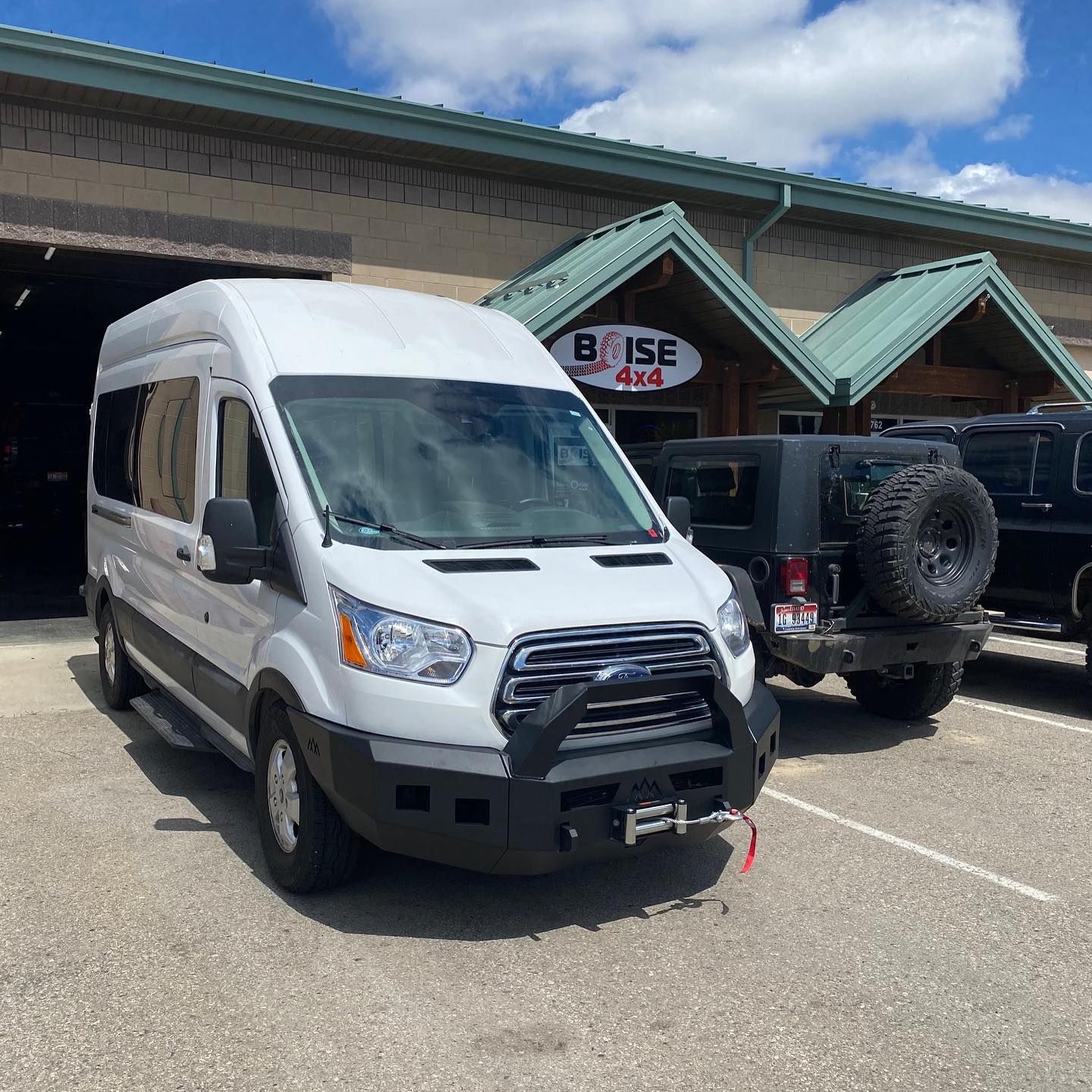 A white Ford Transit van with a heavy-duty off-road bumper parked in front of a Boise 4x4 shop.