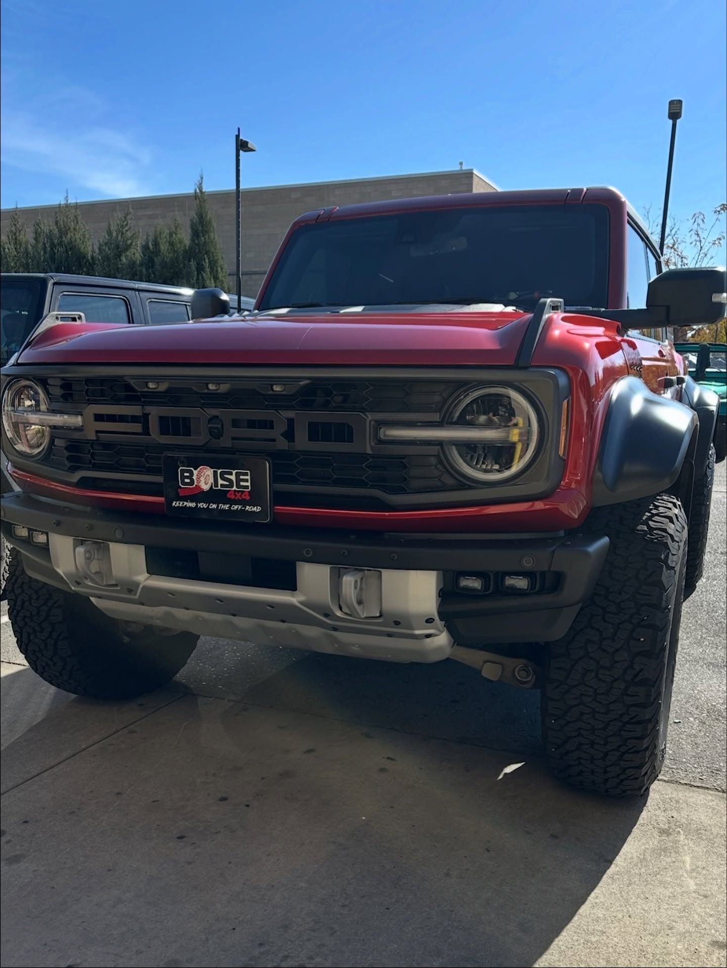 A red Ford Bronco Raptor parked on an asphalt lot under a bright blue sky.