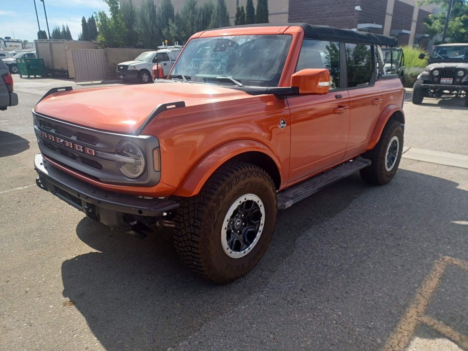 An orange Ford Bronco parked in a sunny outdoor lot, showing its front three-quarter profile and rugged off-road tires.