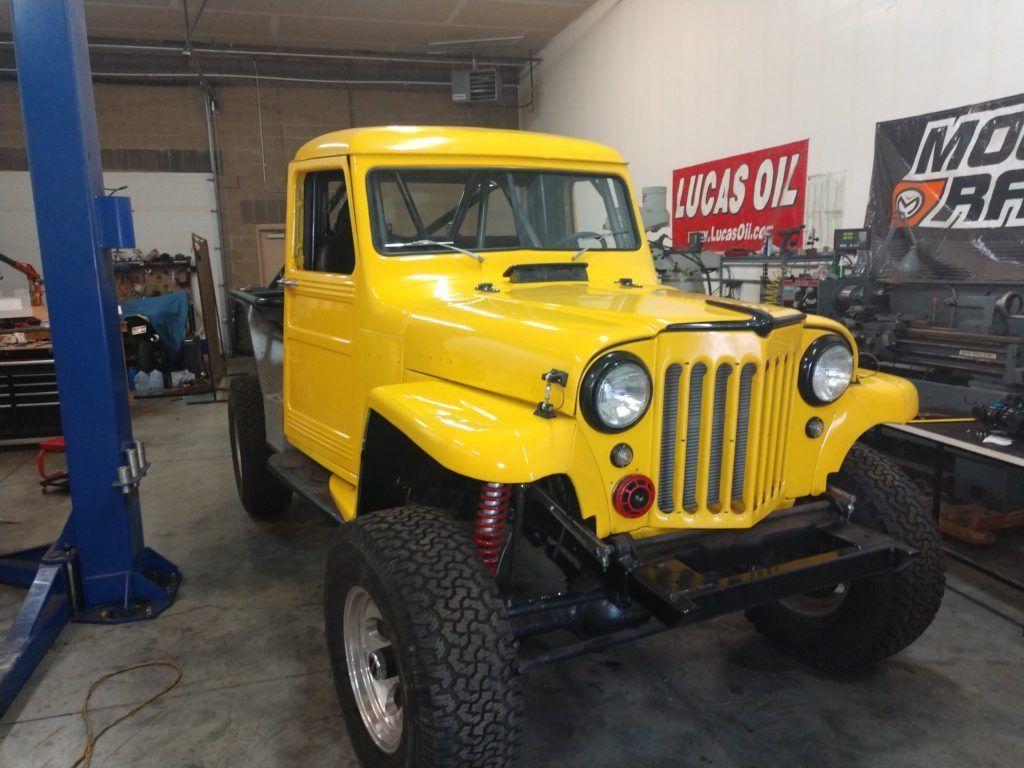 A bright yellow custom Jeep truck parked in a garage next to a blue vehicle lift.