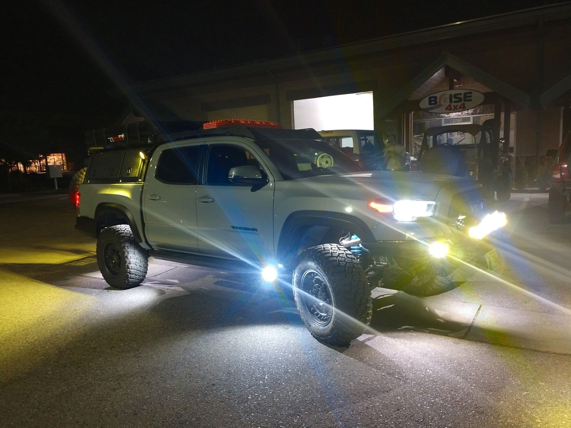 A white Toyota Tacoma pickup truck parked at night with bright LED off-road lights illuminated.