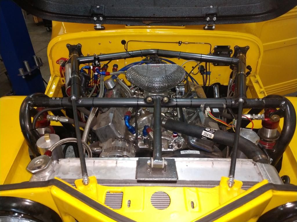 A view into the engine bay of a yellow vehicle, featuring a prominent black tubular chassis brace and a central air filter.