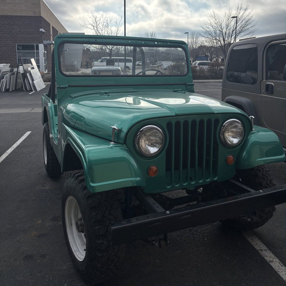 A modified Jeep with large off-road tires parked in a parking lot, with its front driver-side wheel on a metal ramp.