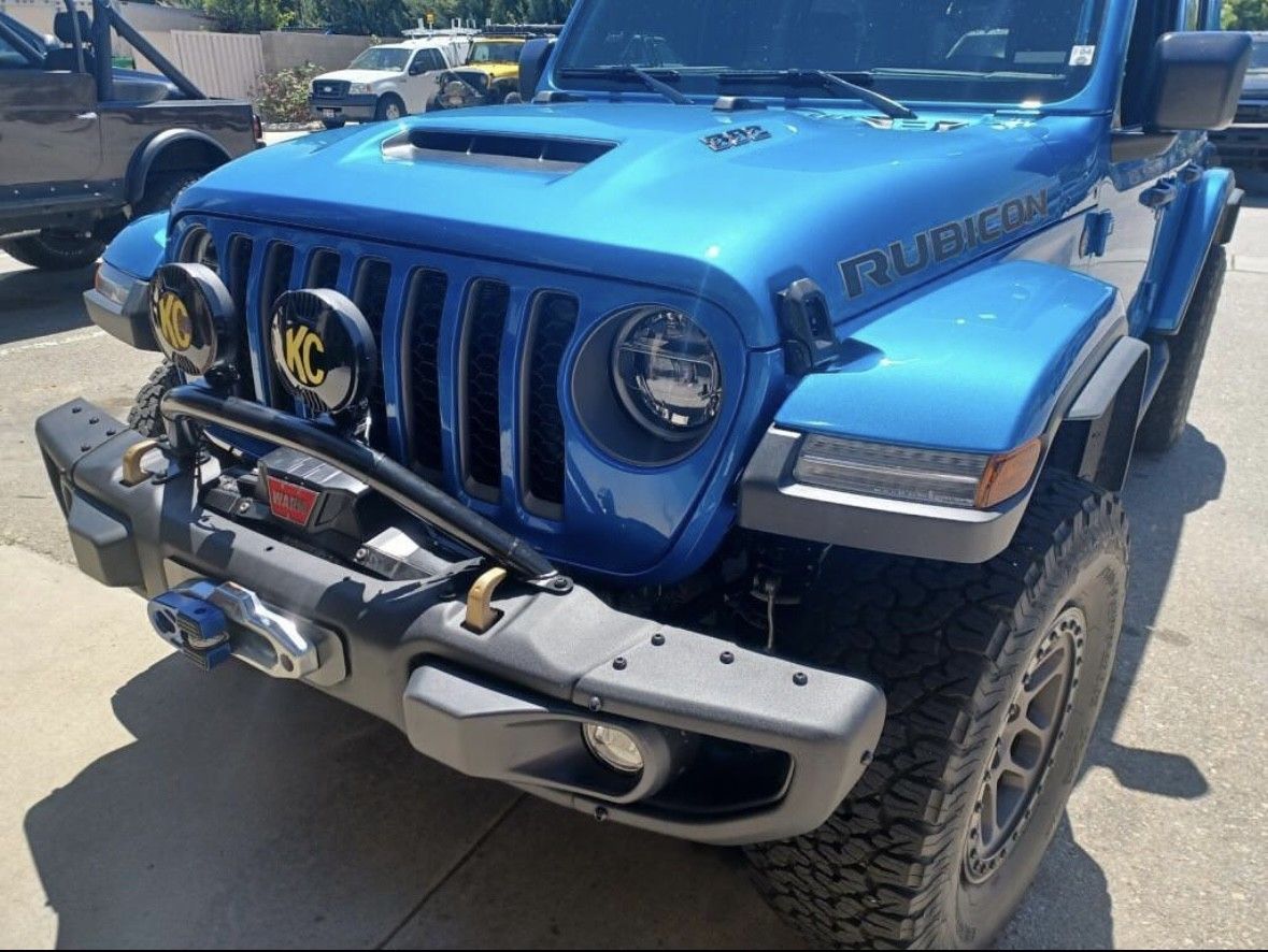 A bright blue Jeep Rubicon with off-road lights and a winch parked on a sunny day.