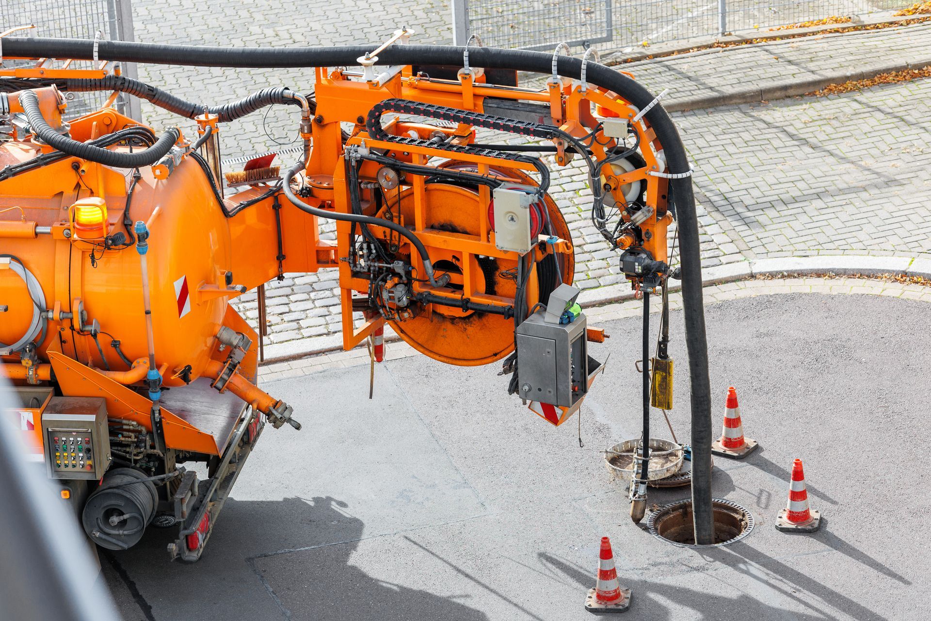 Orange sewer vacuum truck cleaning a manhole in a paved street.
