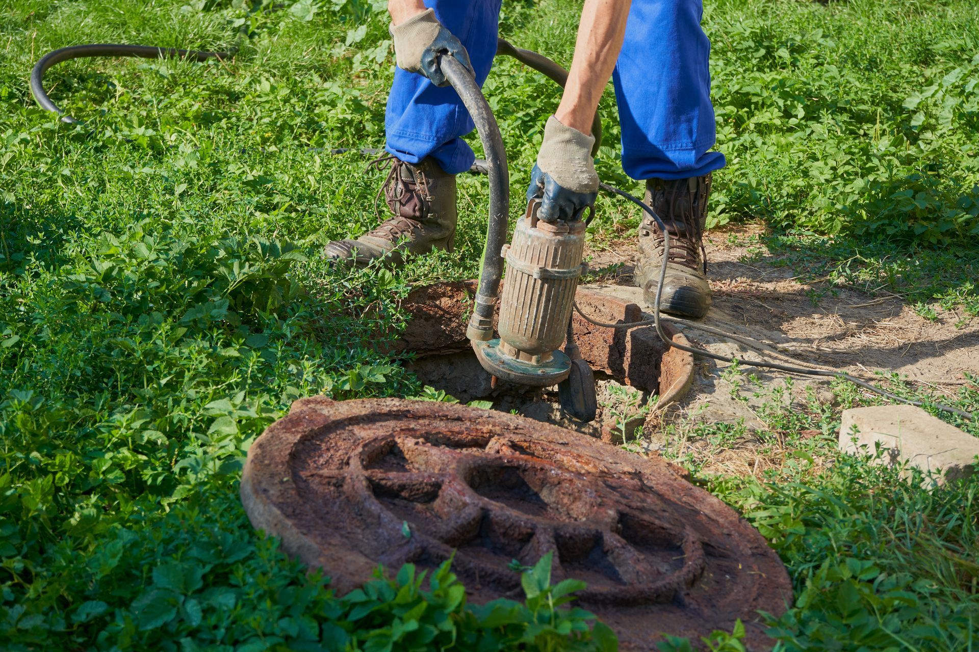 Person using a jackhammer on the ground, with a stone carving nearby. Green grass surrounds. Person using a jackhammer on the ground, with a stone carving nearby. Green grass surrounds.