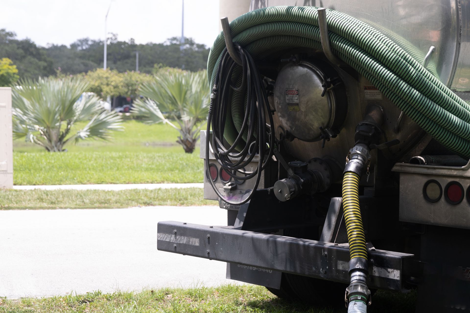 A close-up of a septic tank truck parked on a street full of green foliage.