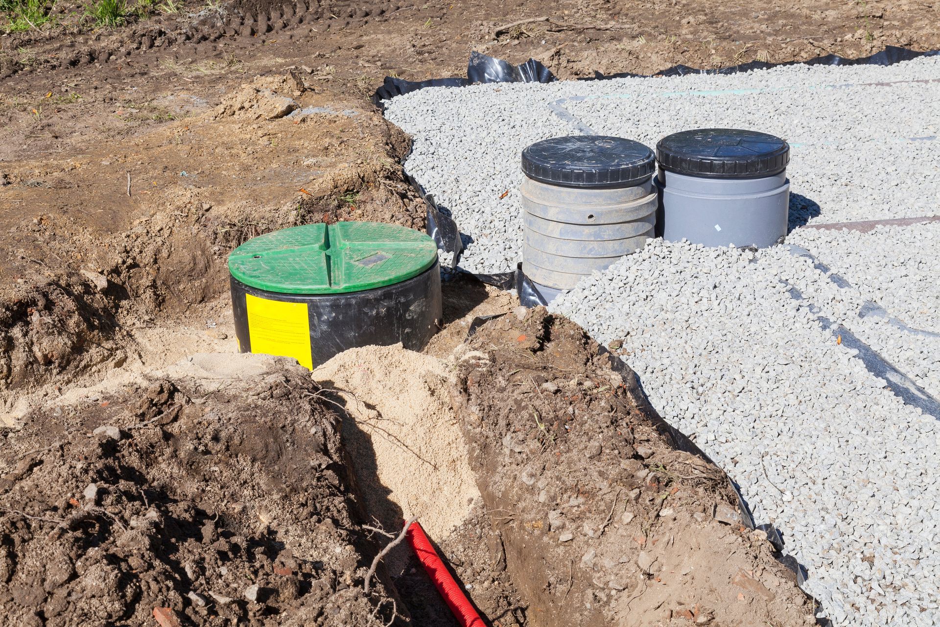 Excavation with three capped septic system components; two gray and one green, in gravel.