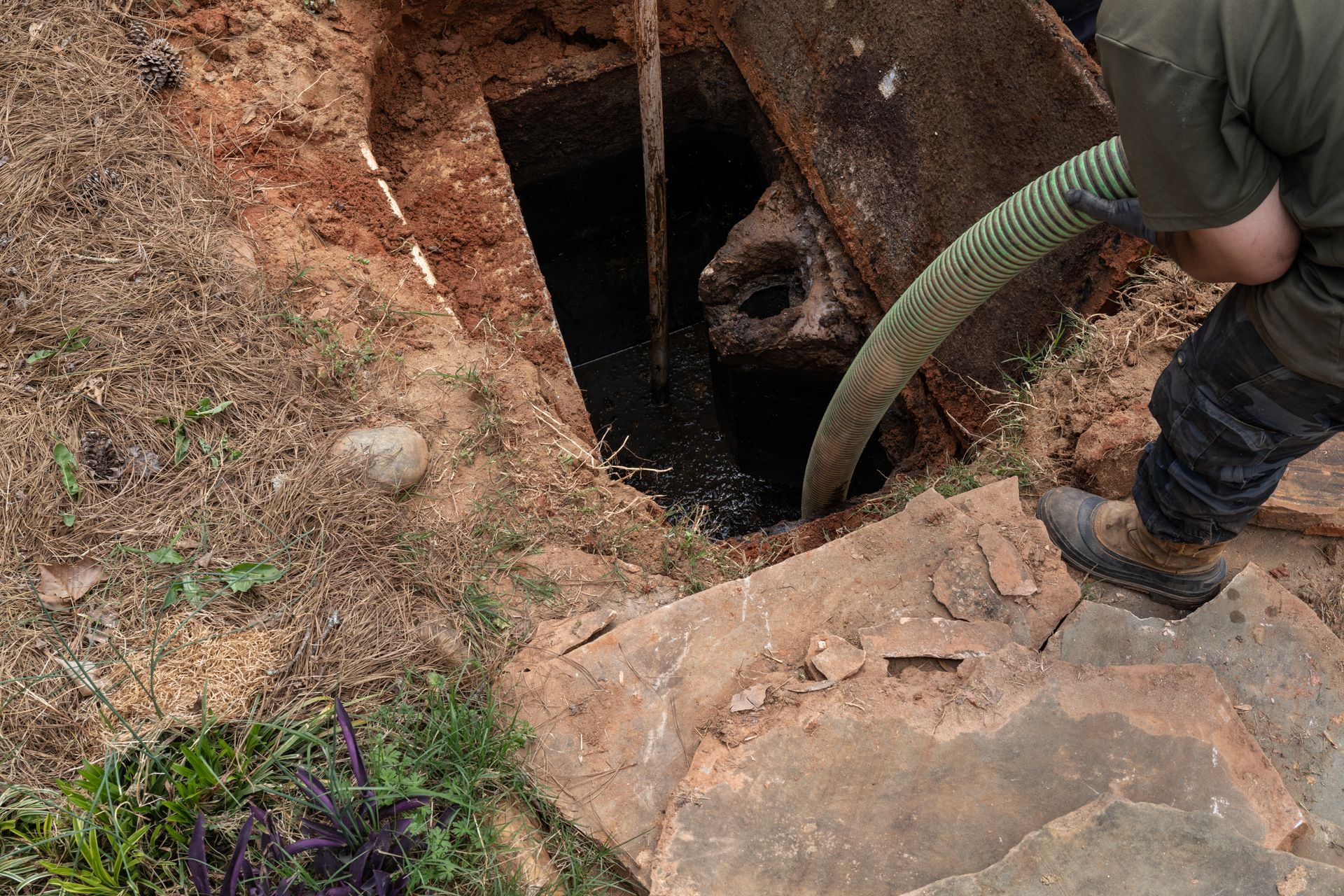 Person pumping waste from a septic tank in an outdoor setting. Person pumping waste from a septic tank in an outdoor setting.
