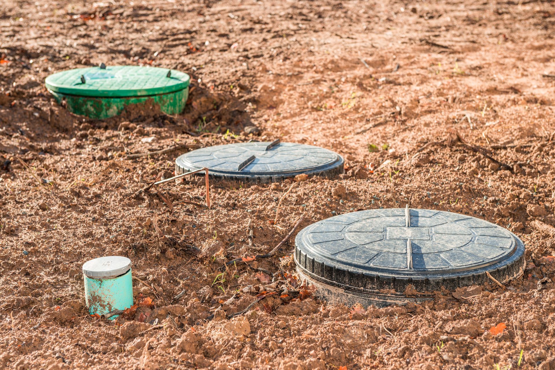 Three septic tank lids and a small pipe in dirt. The lids are green and gray. Three septic tank lids and a small pipe in dirt. The lids are green and gray.