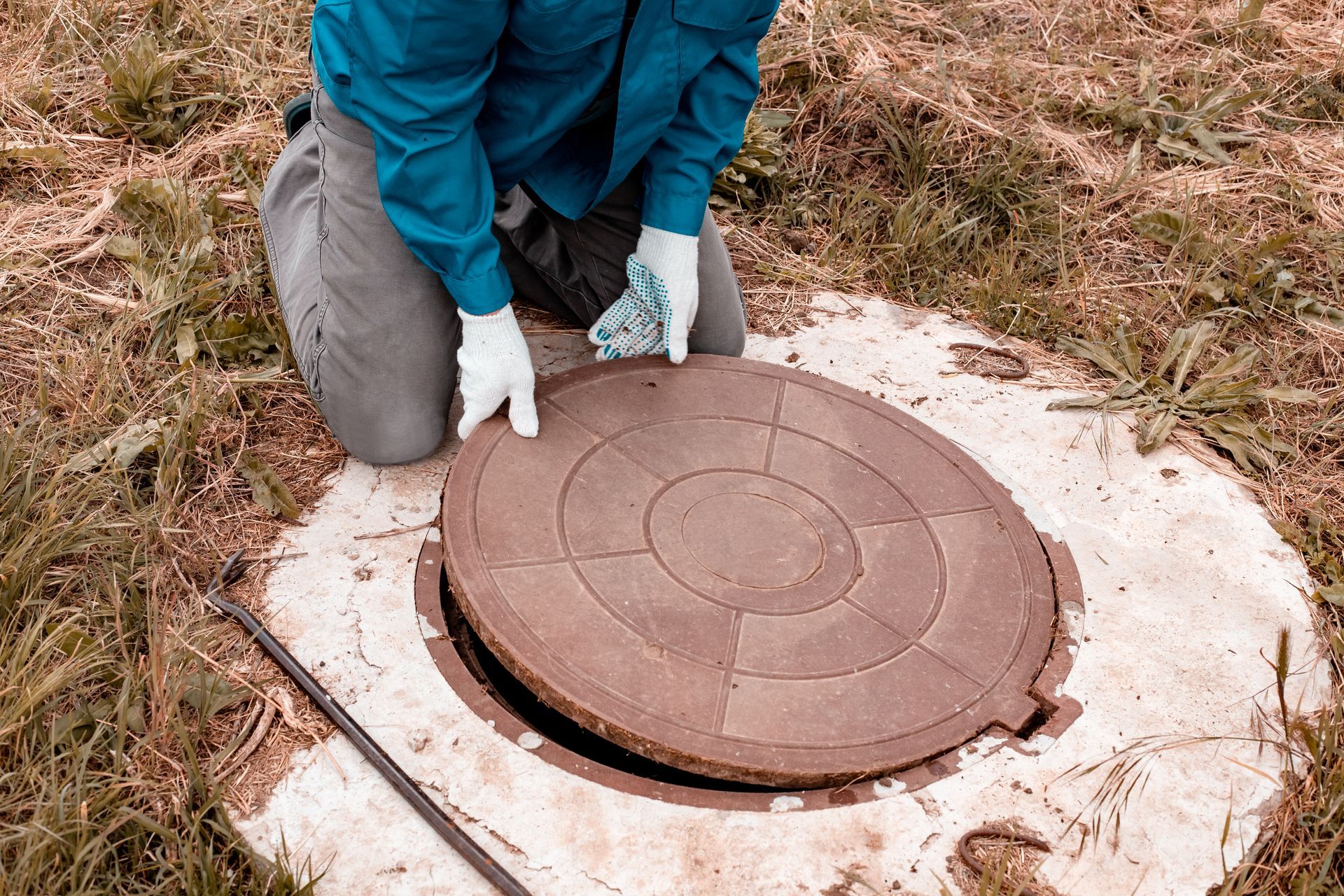 Person kneeling, lifting a circular manhole cover in a grassy area. Person kneeling, lifting a circular manhole cover in a grassy area.