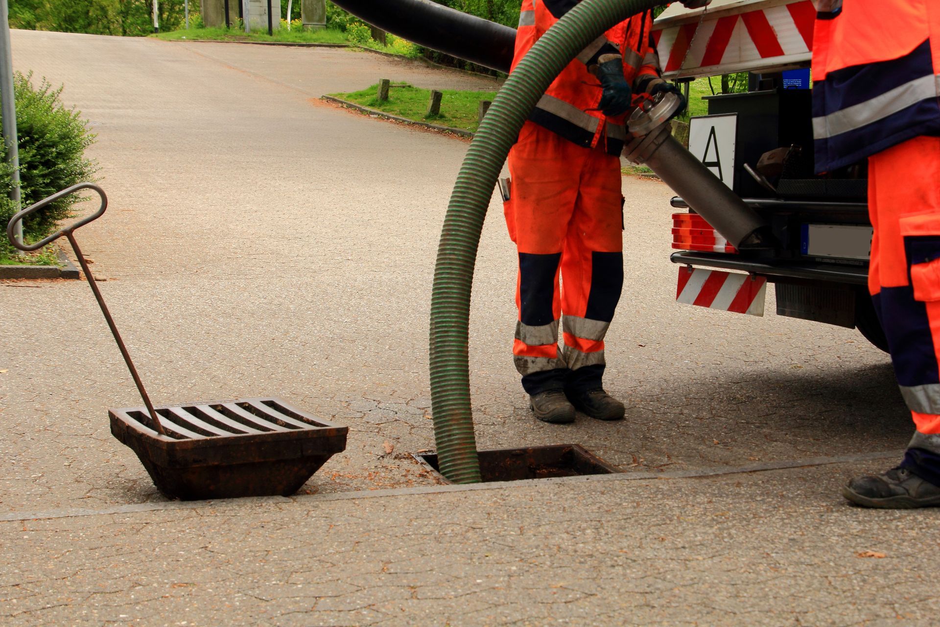 Workers in orange suits clean a sewer grate with a large hose, truck in background. Workers in orange suits clean a sewer grate with a large hose, truck in background.