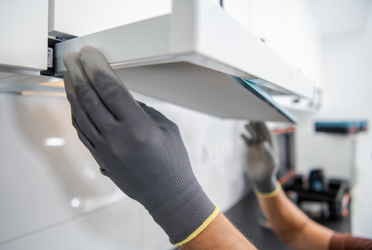 Person with grey gloves installing a white range hood in a kitchen.