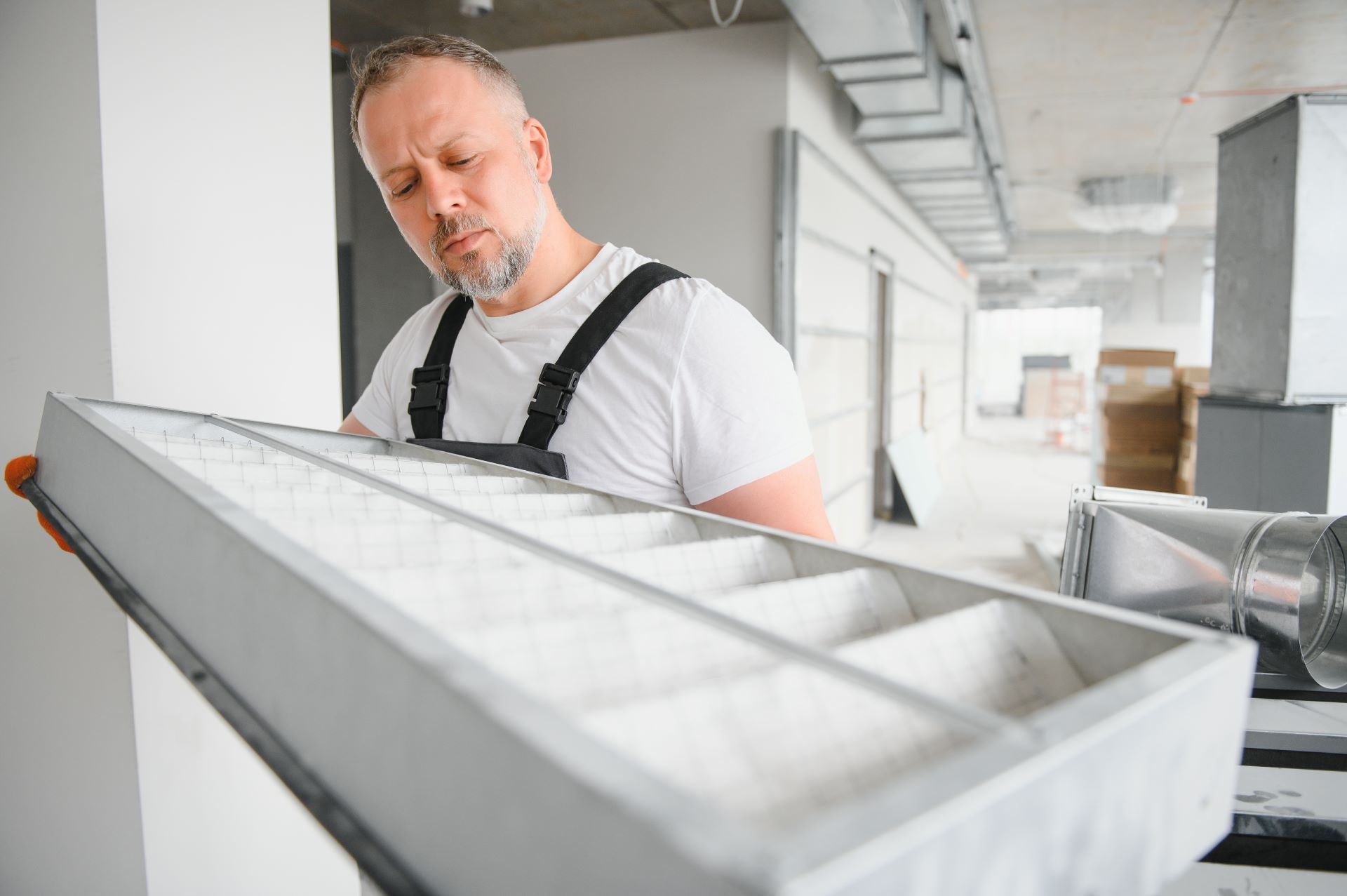 Man in overalls inspecting an air filter in a construction setting.