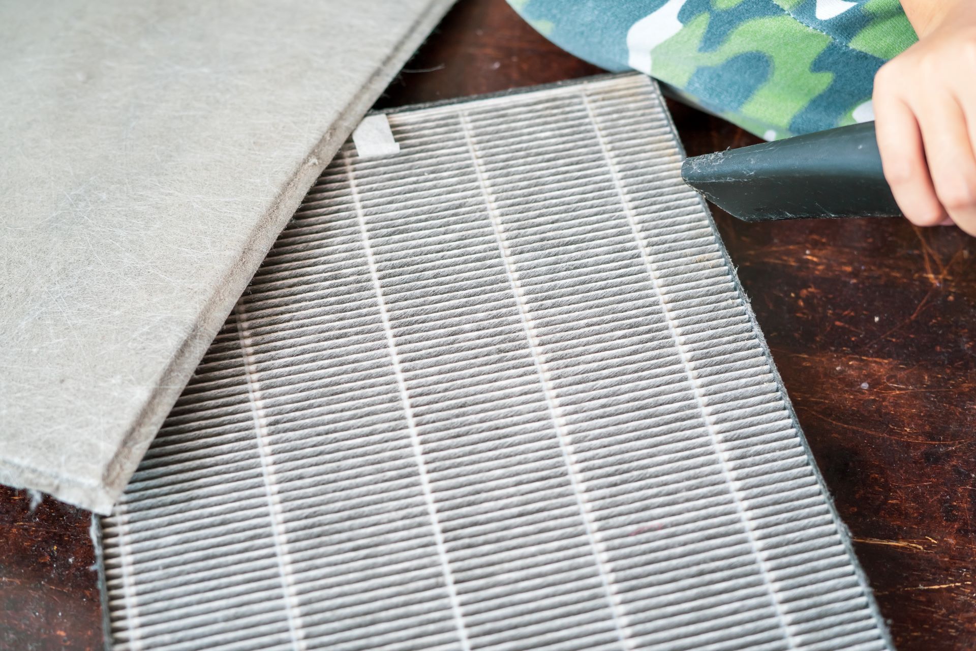 Dirty air filter and hand holding a small brush, next to a gray, textured surface.