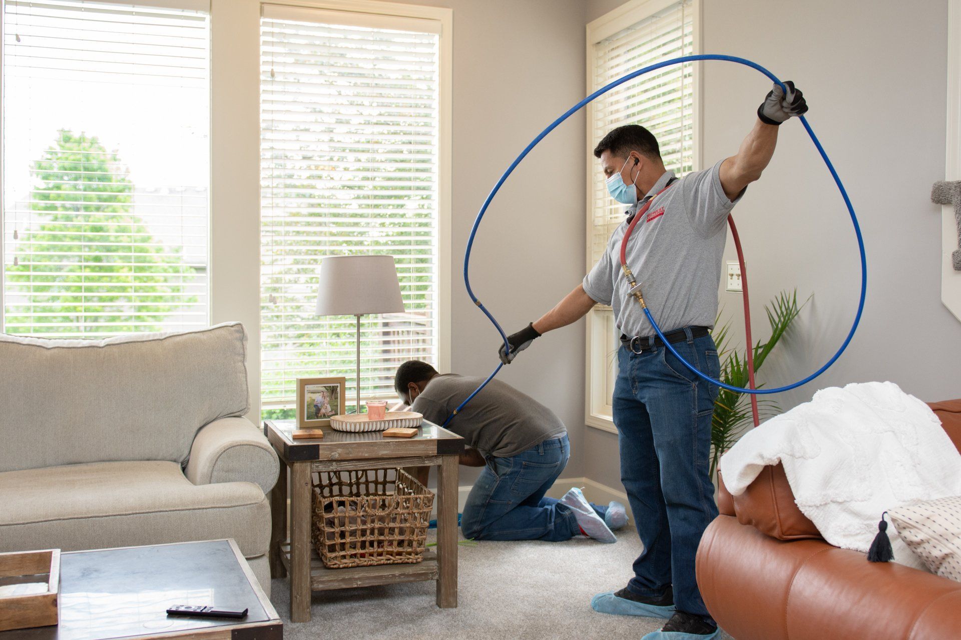 Two men cleaning carpet in a living room. One sprays water, the other inspects the floor.