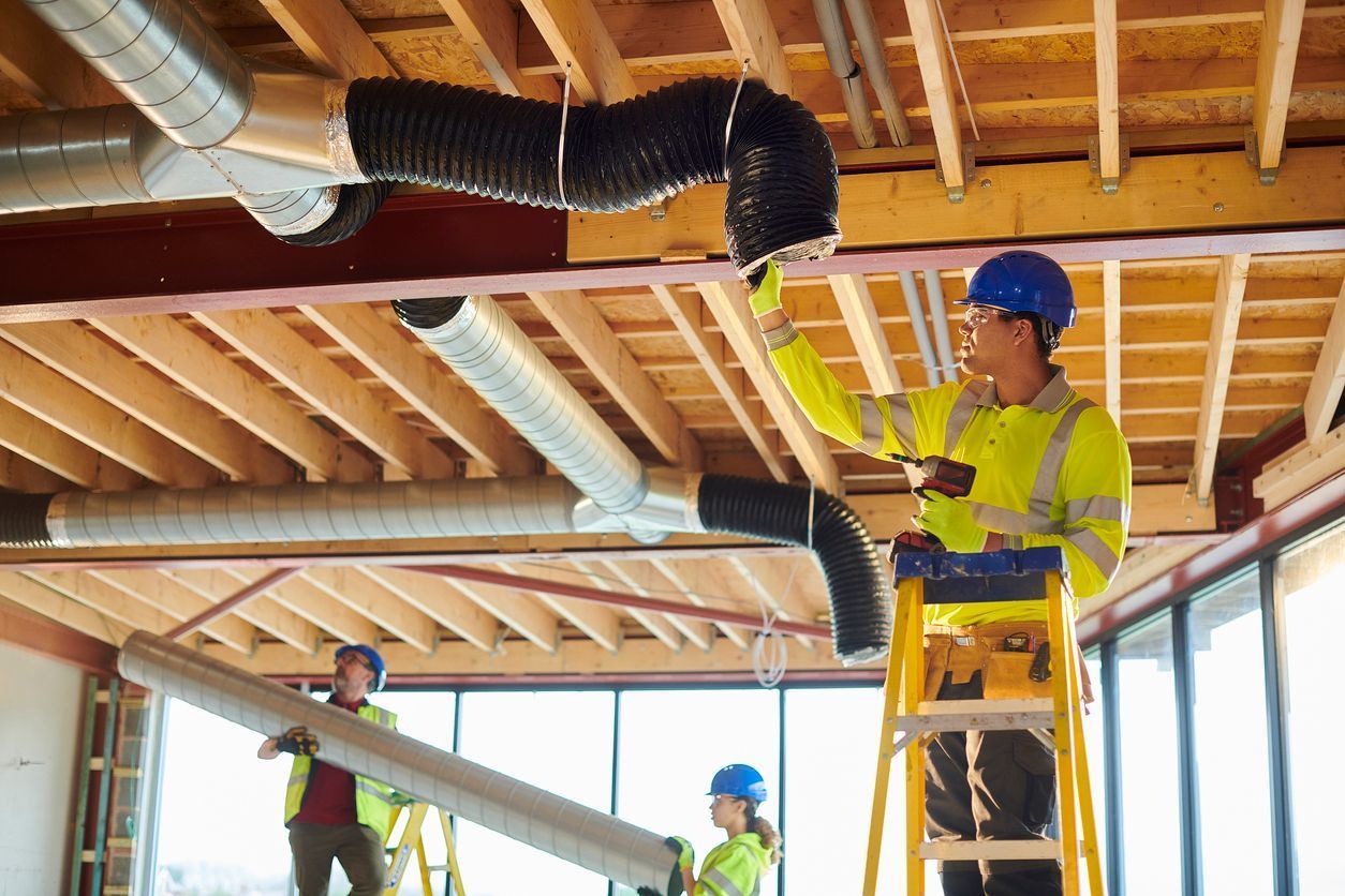 Construction workers installing ductwork in a building. One on a ladder, others holding materials.