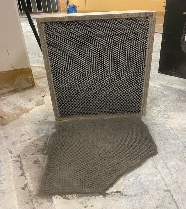 Wooden frame with metal mesh filter and a detached piece of mesh, sitting on a concrete floor.