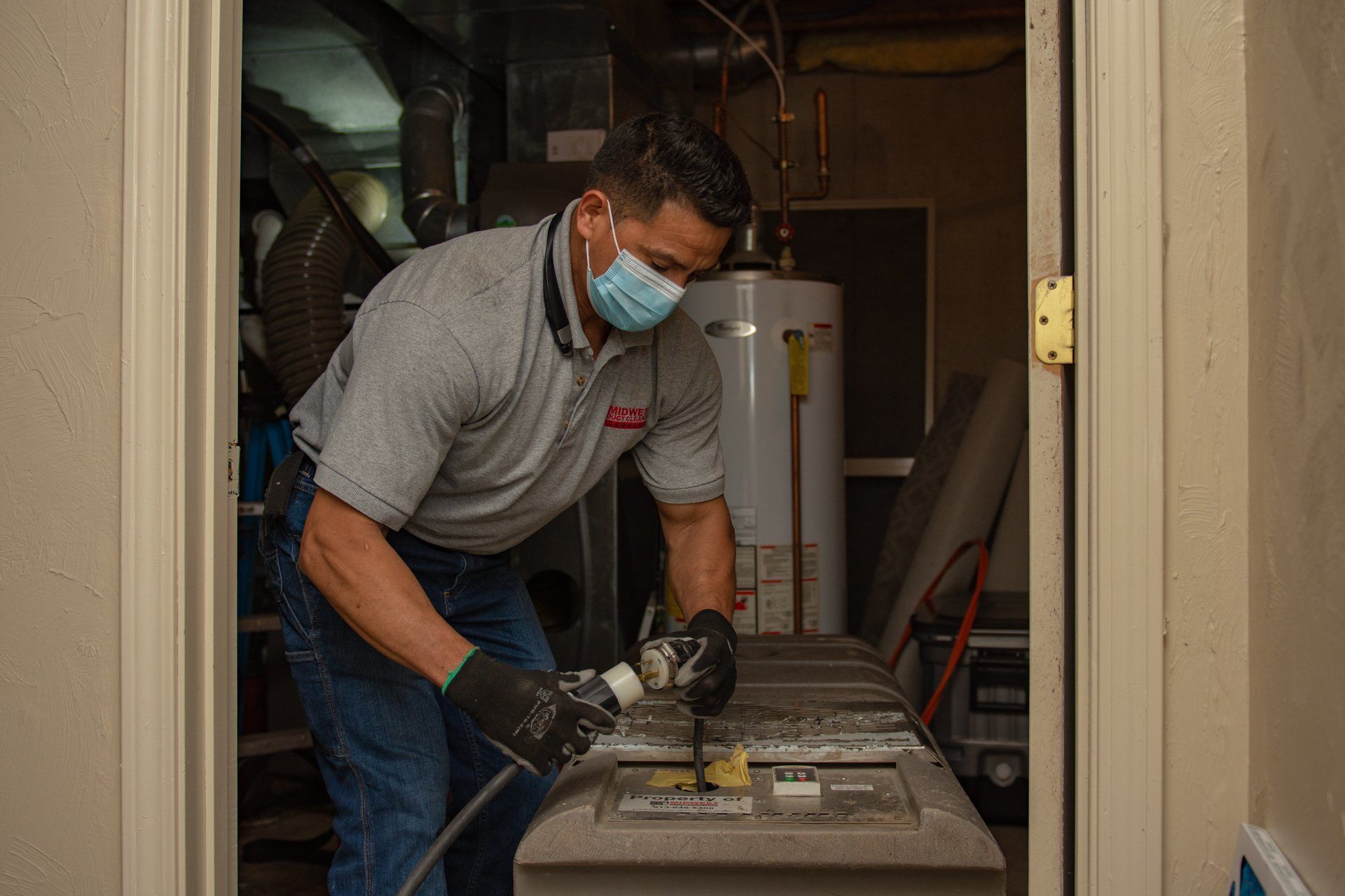 Man in mask cleans a furnace in a utility room.