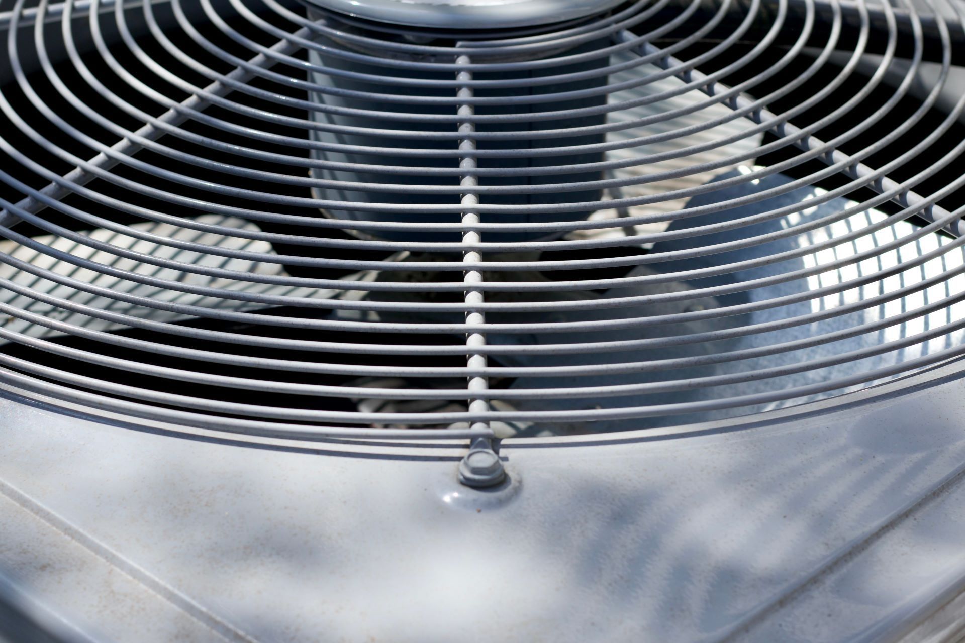 Close-up of an air conditioner fan with protective metal grill.