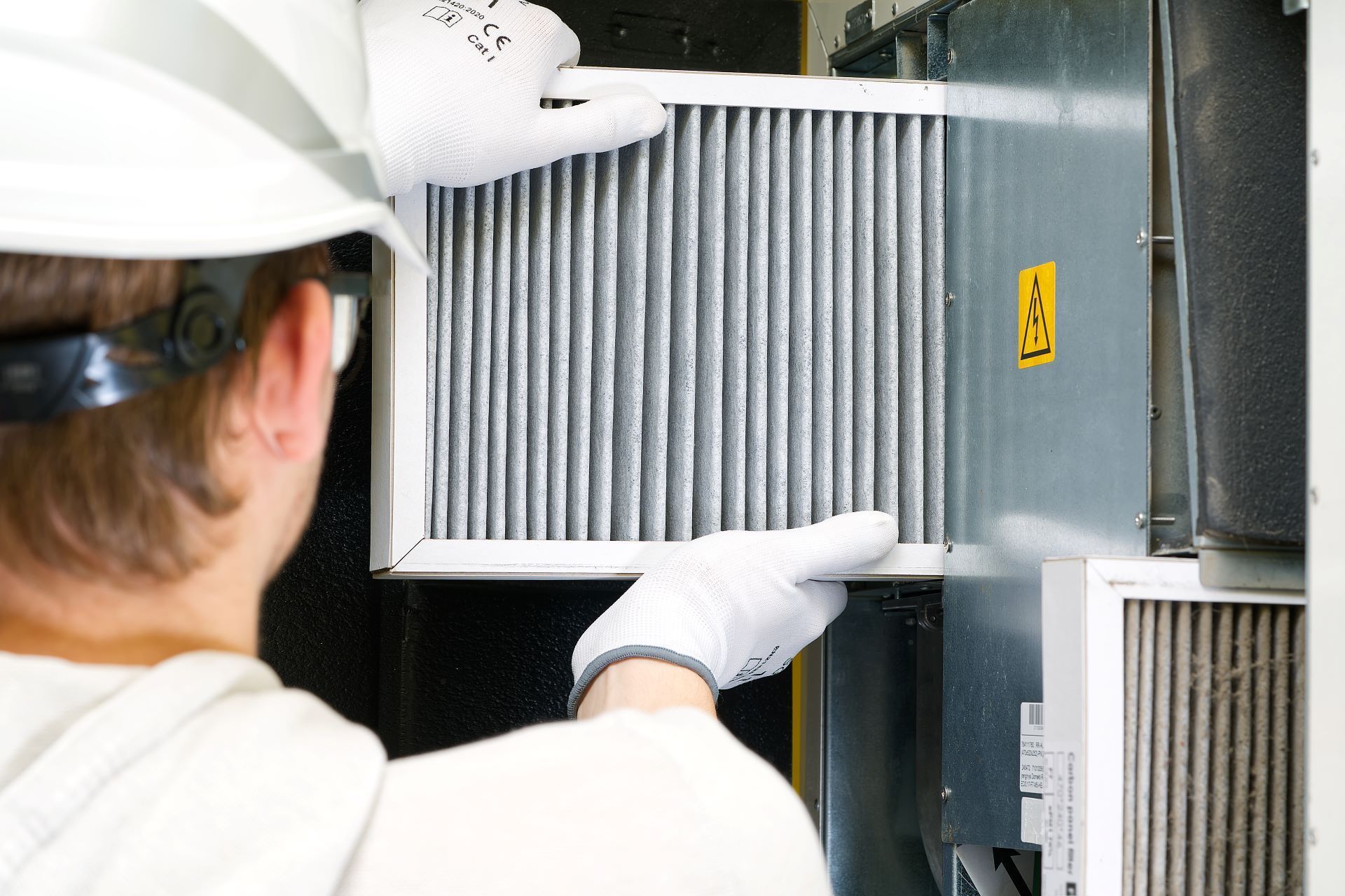 Person in hard hat and gloves replacing an air filter in an HVAC system.