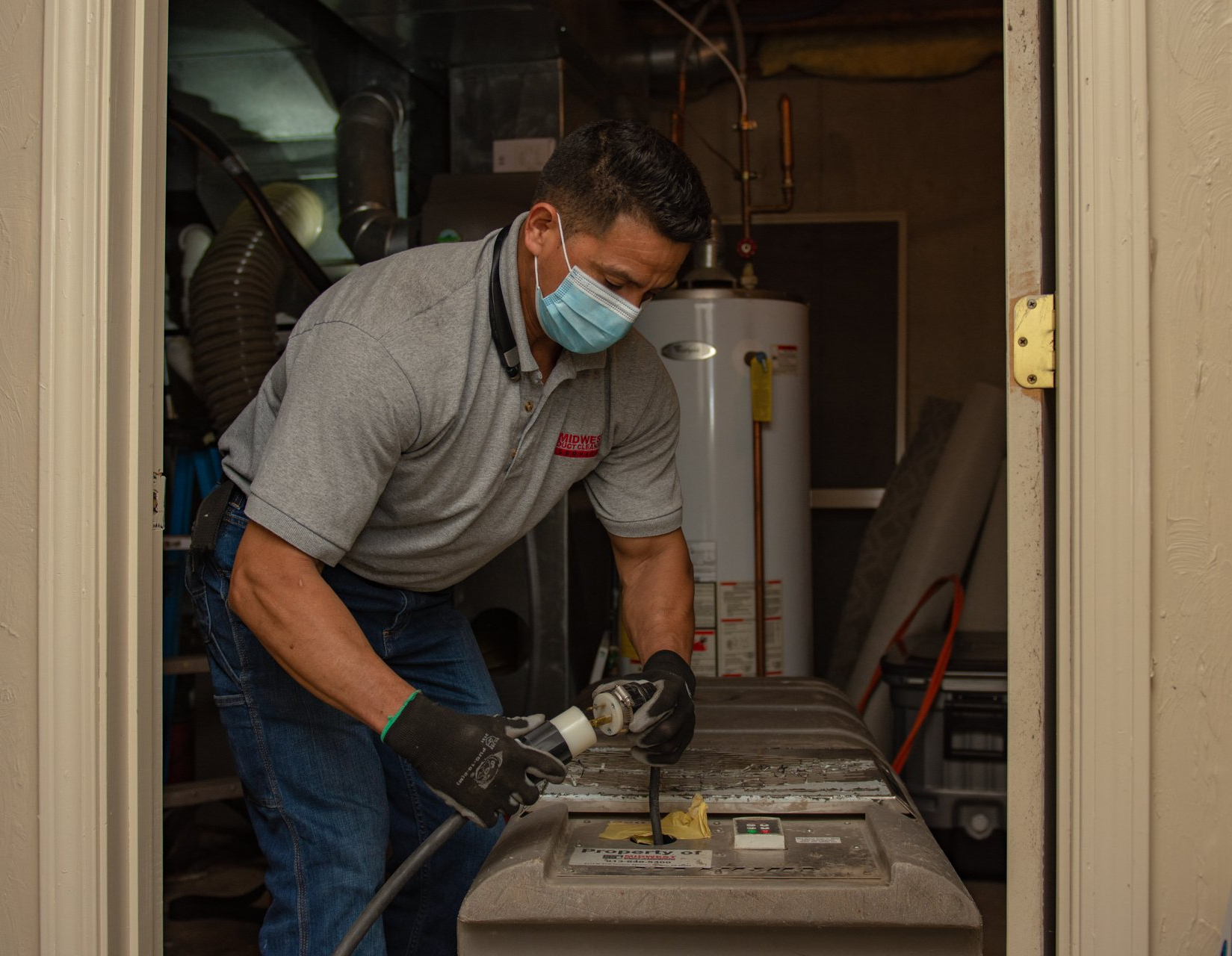 Man in mask cleaning HVAC system in a basement.