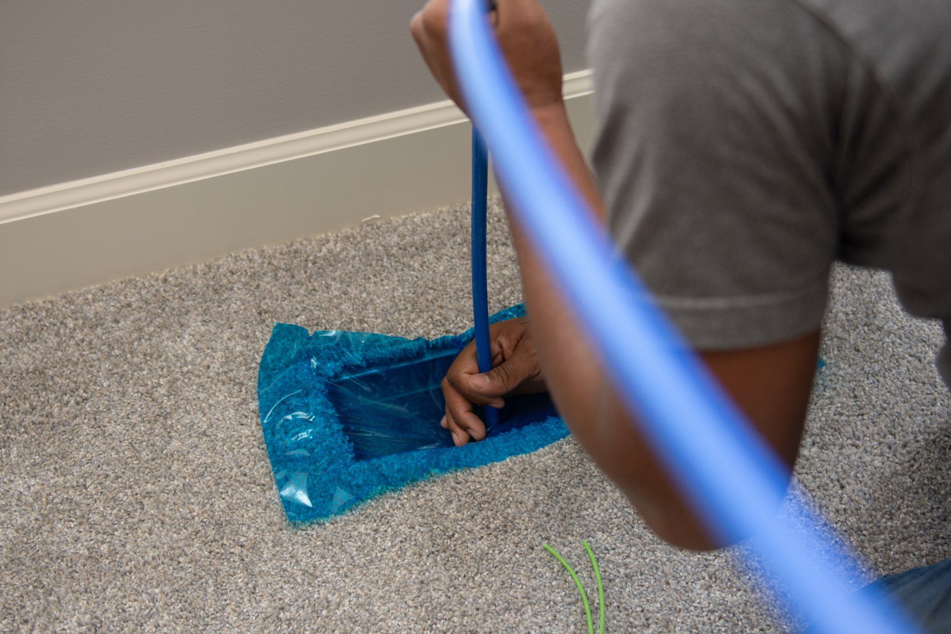 Person kneeling on carpet, inserting a blue tube into a blue plastic bag.