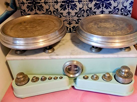 Antica bilancia con due vassoi circolari, base verde menta e pesi.