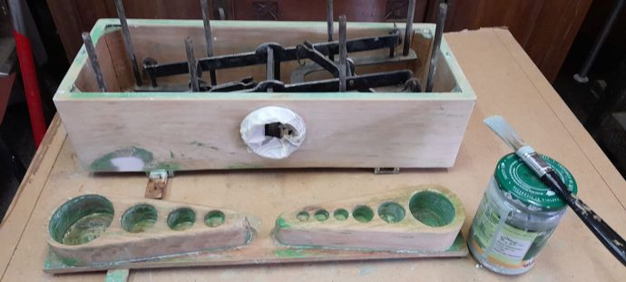 Scatola di legno con componenti in metallo, due vassoi con fori circolari e materiali per la pittura.