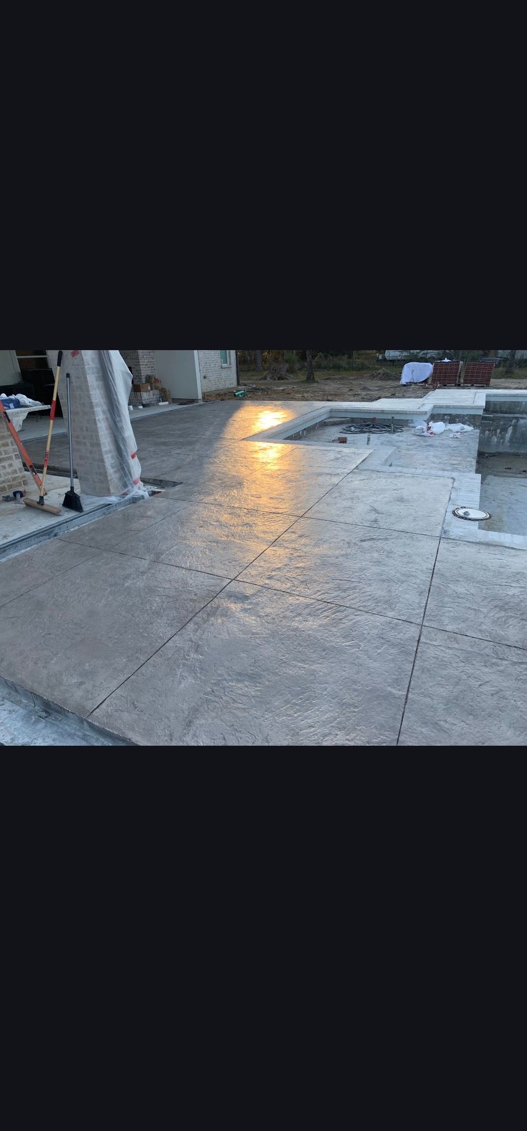 Wet concrete sidewalk with a bright reflection near a building entrance and parked items nearby
