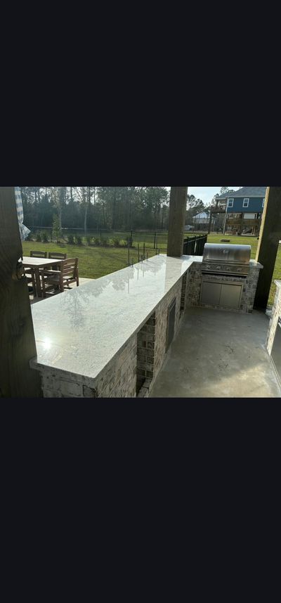 Long outdoor concrete table with benches in a park or patio, beside a lawn and trees