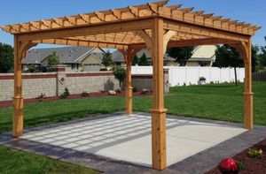 Wooden pergola over a concrete patio in a landscaped backyard, with lawn, wall, and house in the background