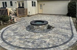 Backyard stone patio with a circular fire pit and garage in the background