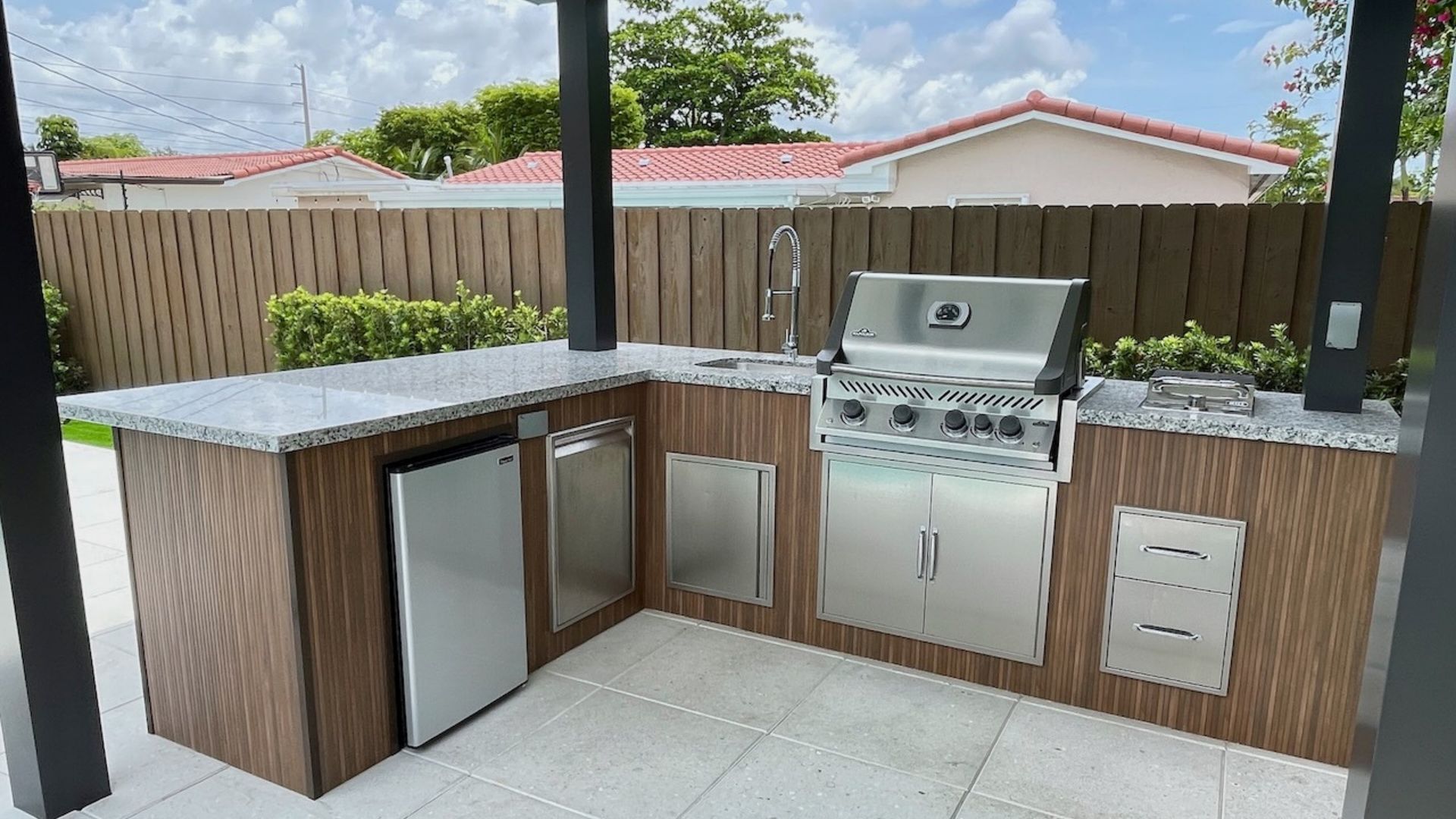 Outdoor kitchen with grill, sink, and cabinets on a tiled patio