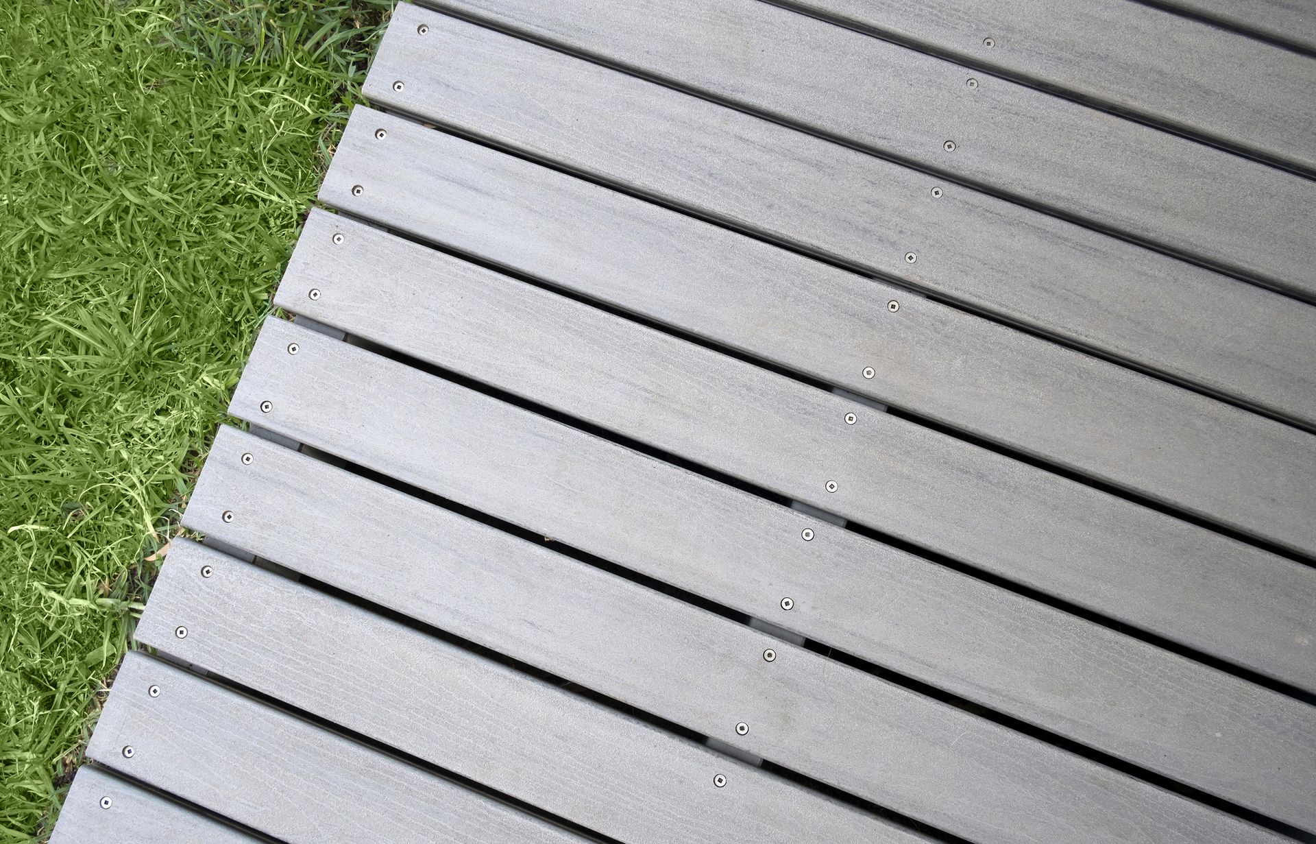 Gray wooden deck beside green grass in a diagonal view
