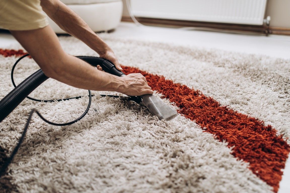 Person cleaning a rug with a carpet cleaner. Beige rug with a red stripe.